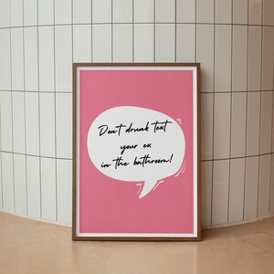 May include: Pink framed poster with a white speech bubble that says "Don't drunk text your ex in the bathroom!"