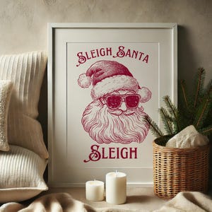 May include: A white framed print with a red illustration of Santa Claus wearing sunglasses and the text "Sleigh Santa Sleigh".