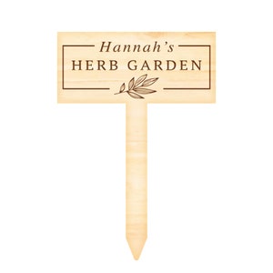 May include: A wooden garden marker with the text "Hannah's HERB GARDEN" and a small leaf design. The marker is brown and has a pointed end.