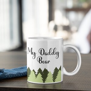 May include: White ceramic mug with a black and green design. The mug has the text "My Daddy Bear" printed on it.