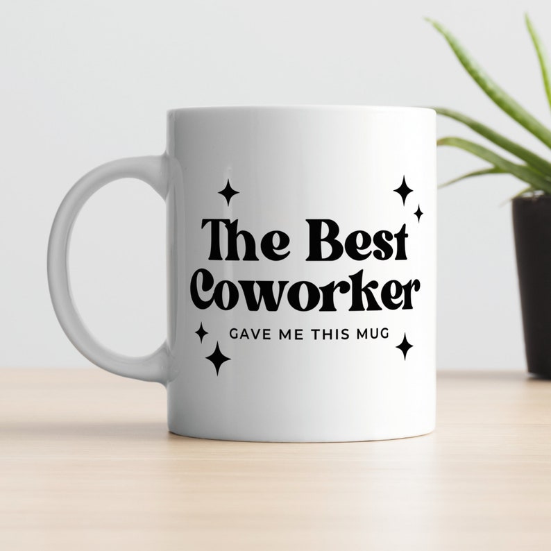 Op de afbeelding: Witte keramische mok met zwarte tekst die "The Best Coworker Gave Me This Mug" luidt met kleine sterren aan weerszijden van de tekst.
