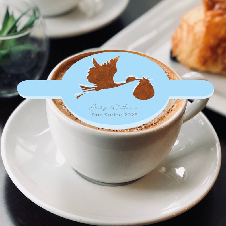 May include: A white coffee mug with a blue and brown stork design. The mug has the text "Baby William Due Spring 2025" on it.