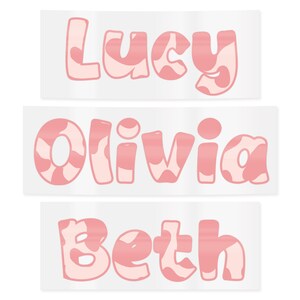 May include: Three stickers with the names "Lucy", "Olivia", and "Beth". Each name is in a bubble letter font with a pink and white cow print design. The stickers are rectangular with a white background.