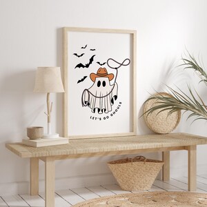 May include: A white ghost wearing a cowboy hat and holding a lasso with the text "Let's go ghouls". The ghost is surrounded by bats.
