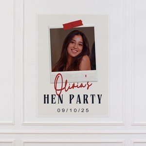 May include: A white poster with a photo of a woman, red tape, and text. The text reads "Olivia's HEN PARTY" and "09/10/25". The photo is in a white frame.
