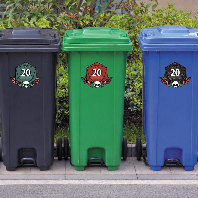 May include: Three colorful trash cans: black, green, and blue. Each has a decorative sticker featuring a twenty-sided die, flowers, and a skull. The cans are lined up on a concrete surface with greenery in the background.