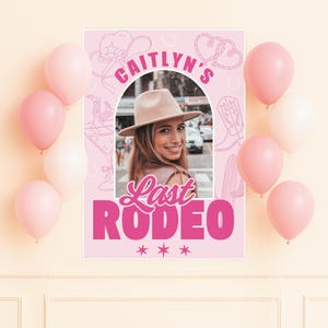 May include: A pink poster with the text "Caitlyn's Last Rodeo" and a photo of a woman wearing a hat. The poster is decorated with cowboy-themed illustrations and surrounded by pink and white balloons. The poster is a party decoration.