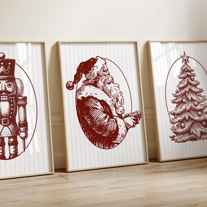 May include: Three framed Christmas-themed prints. The prints feature a nutcracker, Santa Claus, and a Christmas tree, all in a vintage red and white color scheme. The artwork is set against a white background with vertical stripes.