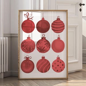 Op de afbeelding: Een ingelijste print met negen rode kerstballen met diverse patronen. De ballen zijn rond en hebben ontwerpen zoals strepen, krullen en stippen. De print zit in een houten lijst, geschikt voor feestelijke decoratie.