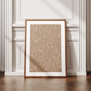 Op de afbeelding: Een ingelijst print met een minimalistisch ontwerp met een patroon van witte lijntekeningen van gezichten op een bruine achtergrond.