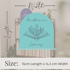 May include: A turquoise blue bookend shaped like an open book with flowers growing out of it. The bookend is 15 cm long and 14.3 cm wide. The text "Anastasia's Library" is written on the bookend.