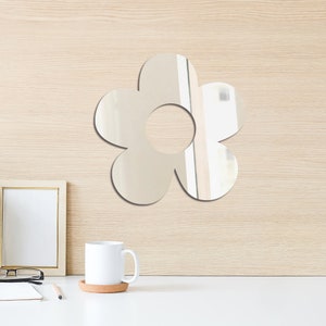May include: A silver flower-shaped mirror with a round center hole. The mirror is mounted on a light wood wall.