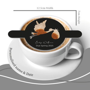 May include: A white coffee mug with a black stencil of a stork carrying a baby. The stencil says "Baby William Due Spring 2025". The mug is 7 cm high and 12.5 cm wide.