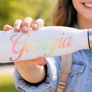 May include: A white ceramic mug with a black handle and the text "But First, Coffee" in a black, handwritten-style font. The mug is on a white surface.