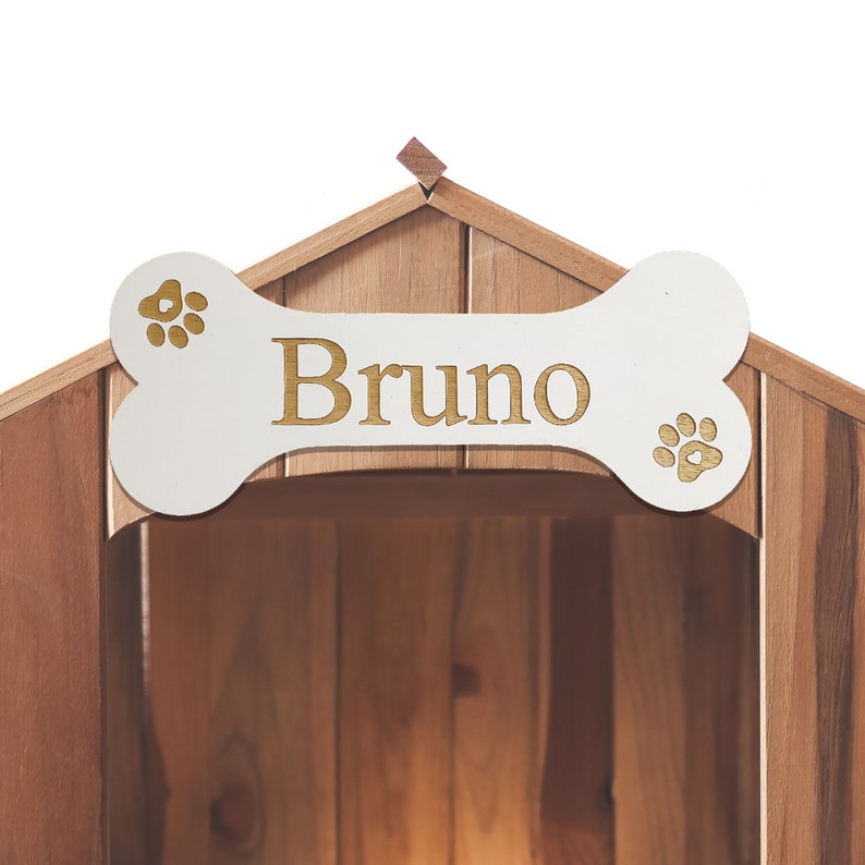 May include: A wooden dog house with a white bone-shaped sign above the entrance. The sign has the name "Bruno" written in gold letters and paw prints on either side.