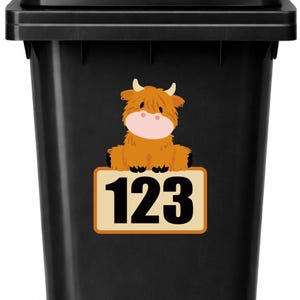 May include: Black trash bin with a sticker featuring a cartoon Highland cow and the number "123" on a rectangular sign. The cow is brown with a pink nose and small horns. The sign has a tan background with an orange border.