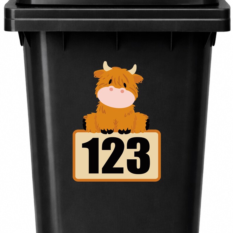 May include: Black trash bin with a sticker featuring a cartoon Highland cow and the number "123" on a rectangular sign. The cow is brown with a pink nose and small horns. The sign has a tan background with an orange border.