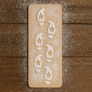 May include: A rectangular, light brown cutting board with a dusting of white powder. Footprints with star cutouts are imprinted in the powder, creating a whimsical design. The board rests on a wooden surface, with additional powder scattered around.