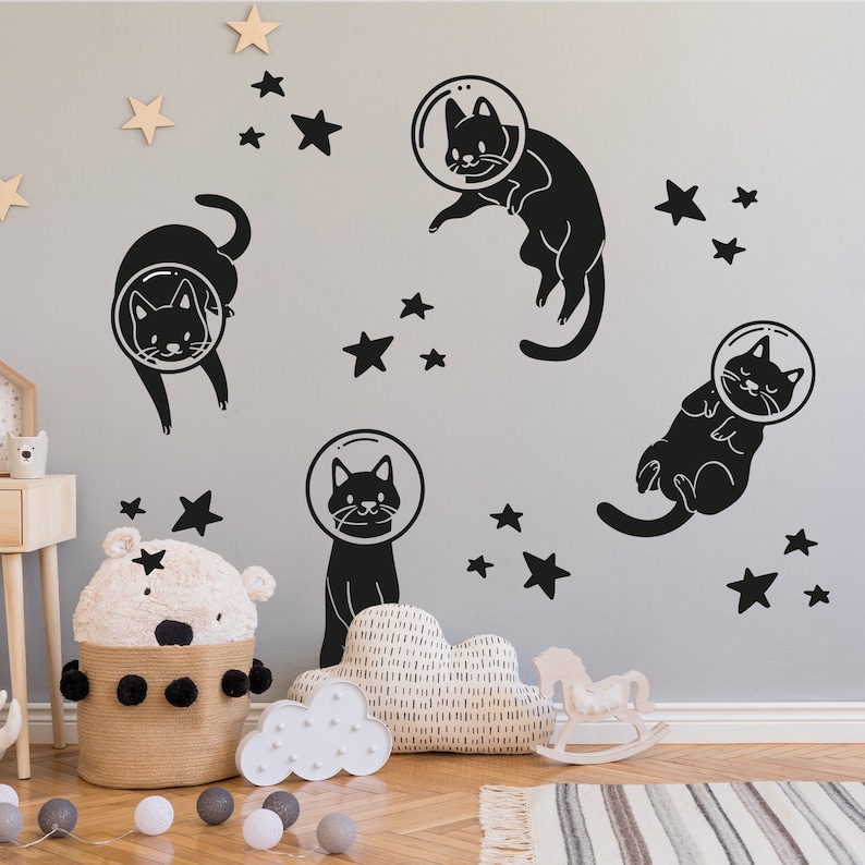 Pode incluir: Adesivos de parede preto e branco com gatos usando capacetes de astronauta e estrelas. Os adesivos est&atilde;o em uma parede cinza claro.