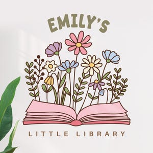 May include: A logo for "Emily's Little Library" features a pink open book with colorful flowers and greenery sprouting from it. The text "EMILY'S" is in green above the flowers, and "LITTLE LIBRARY" is below.