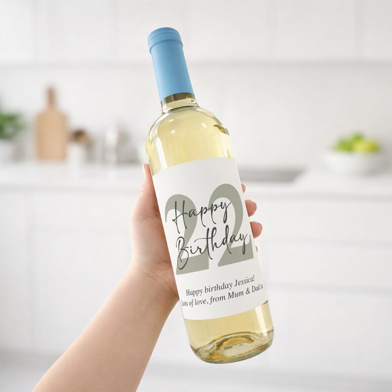 May include: A clear wine bottle with a light blue cap and a white label. The label reads "Happy Birthday" with the number "22" in a large font. The text "Happy birthday Jessica! Lots of love, from Mum & Dad" is also on the label.