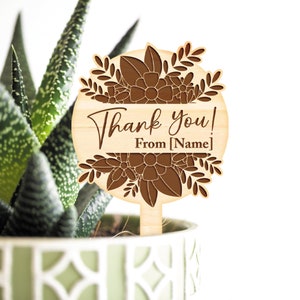 May include: Wooden thank you plant stake with a floral design and the text "Thank you! From [Name]" in brown lettering.