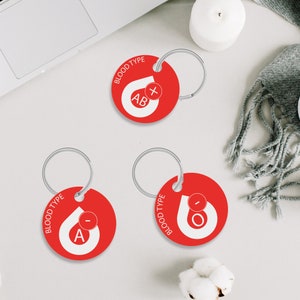 May include: Three red keychains with silver rings. Each keychain has a white blood drop with a letter and a plus or minus sign. The keychains read "BLOOD TYPE" and "AB+", "A-", and "O-".