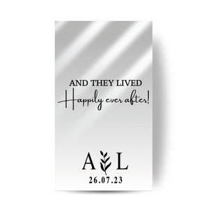 以下が含まれることがあります： 影の効果のある白い背景。テキスト「AND THEY LIVED happily ever after!」は黒色です。テキストの下には、植物の小さなグラフィックが間に挟まれた「A」と「L」の文字があります。日付「26.07.23」は文字の下にあります。