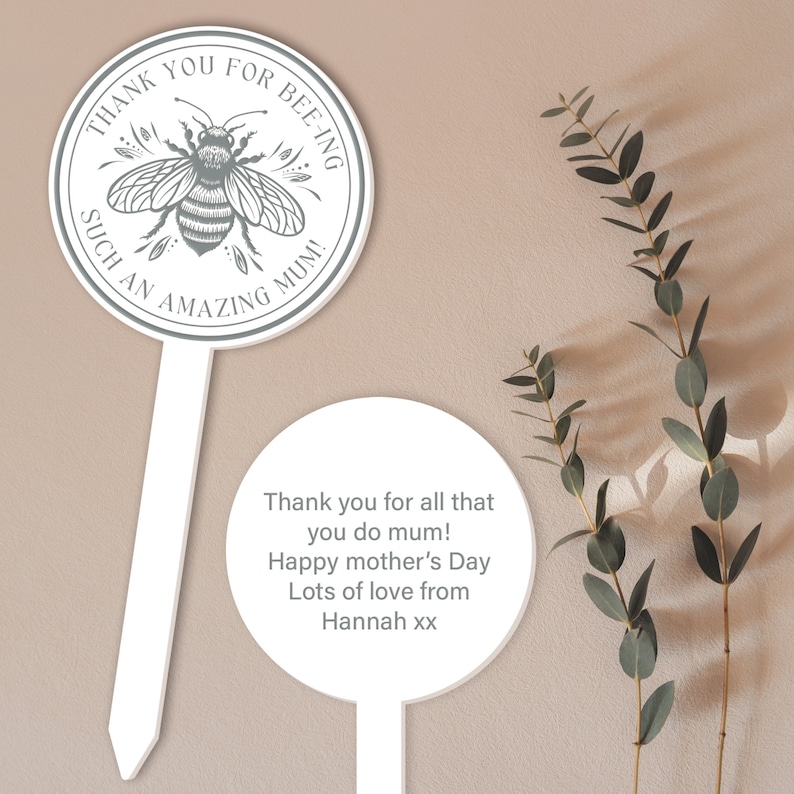 May include: Two white round garden stakes with a bee illustration and the text "Thank you for bee-ing such an amazing mum!" on one stake and the text "Thank you for all that you do mum! Happy mother's Day Lots of love from Hannah xx" on the other stake.