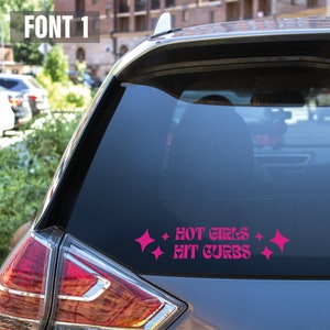 May include: A pink vinyl sticker with the text "HOT GIRLS HIT CURBS" in a retro font. The sticker is on the back window of a gray car.