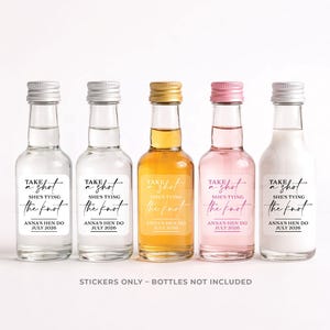 May include: Five small glass bottles with silver, gold, and pink caps, each containing a different colored liquid. The bottles have labels that read "Take a shot, she's tying the knot, Anna's Hen Do, July 2026". The text "Stickers only - bottles not included" is at the bottom.
