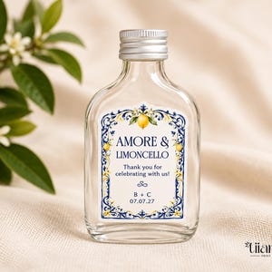 May include: A clear glass bottle with a silver screw cap featuring a rectangular label. The label has a blue and yellow floral border with lemons and the text AMORE & LIMONCELLO, Thank you for celebrating with us!, B + C, and 07.07.27.