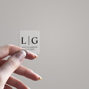 May include: Clear square sticker with black text. The text reads "L|G Lucy & Gareth 15.07.2028".