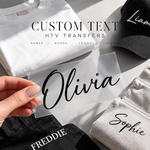 May include: A clear sheet of HTV transfer featuring the name Olivia in a black cursive script font. The image includes a white t-shirt, a black baseball cap with the name Liam, and grey fabric with the name Sophie, plus black fabric with FREDDIE.
