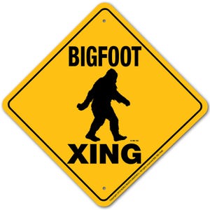 May include: Yellow diamond-shaped warning sign with black text that reads "BIGFOOT XING". A black silhouette of Bigfoot walking is in the center of the sign.