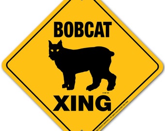 Może przedstawiać: Żółty znak ostrzegawczy w kształcie rombu z czarnym tekstem i sylwetką rysia. Znak informuje "Bobcat Xing" i jest znakiem ostrzegawczym dla kierowców, aby byli świadomi rysi przechodzących przez drogę.