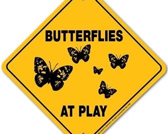 May include: Yellow diamond-shaped sign with black text that reads "Butterflies at Play".  The sign features five black silhouettes of butterflies.