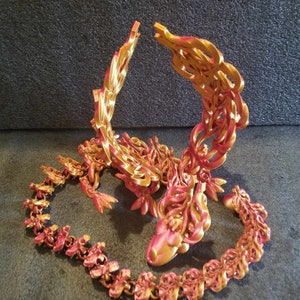 May include: A gold and red 3D printed dragon sculpture with intricate details. The dragon is curled up with its tail in its mouth.