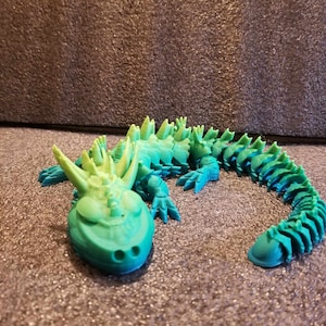 May include: A 3D printed green and blue lizard with a spiky back and a long tail.