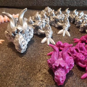 May include: A collection of small, silver and pink dragon figurines. The dragons have detailed scales and horns.