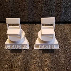 May include: Two white 3D printed miniature chairs on bases. The base on the left has the date "05 AUG 23" printed on it. The base on the right has the initials "FA&FO" printed on it.