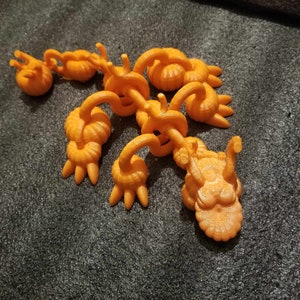May include: An orange 3D printed articulated dragon toy. The dragon has a detailed head and body with multiple joints.