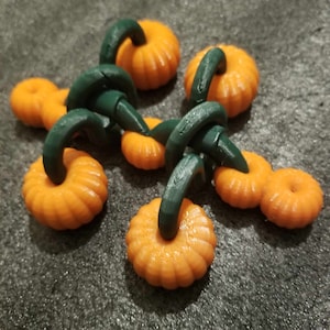 May include: A set of six small, orange pumpkins with green stems, connected together in a vine-like pattern. The pumpkins are all the same size and shape, and they have a slightly textured surface.