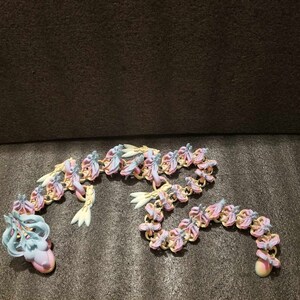 May include: A long chain of pastel pink and blue plastic flowers connected together. The flowers are in the shape of butterflies and are arranged in a wavy pattern.