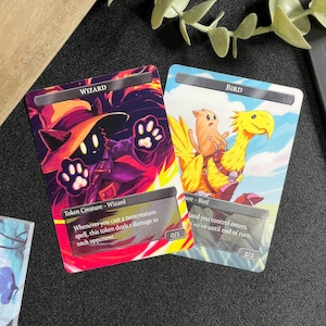 May include: Two fantasy-themed trading card game cards. One card features a wizard with paw-like hands, the other depicts a cat riding a yellow bird. The cards have text that describes their abilities. The wizard card has a 0/1 power/toughness, and the bird card has a 2/2.