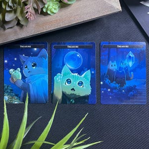 May include: Three blue-toned fantasy art cards featuring adorable cat illustrations. Each card has the word "TREASURE" at the top. One cat holds a small creature, another reaches for a bubble, and the third is with two other cats.