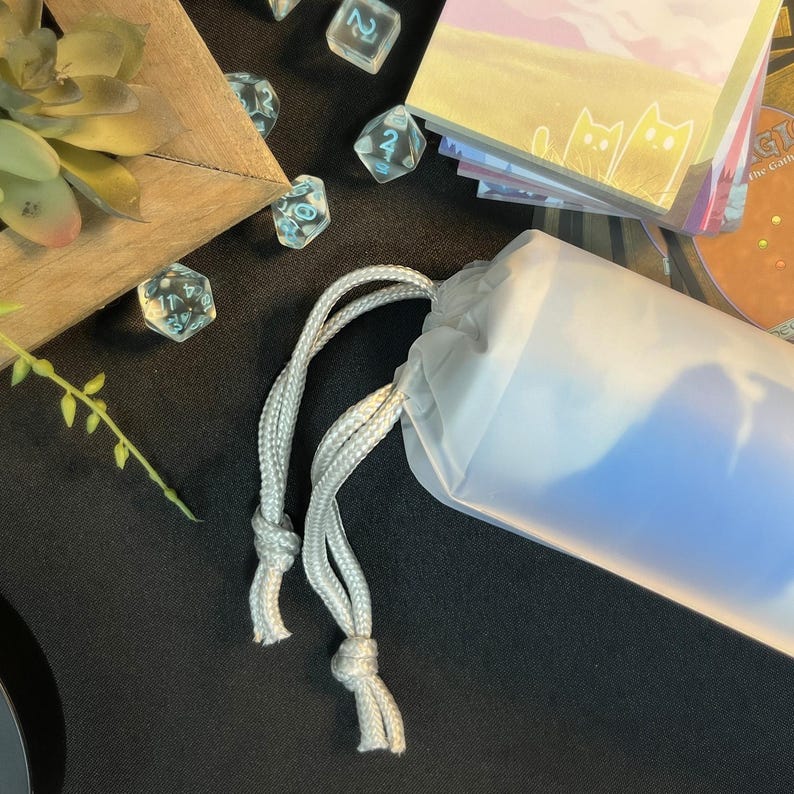 May include: A white drawstring bag with a blue interior. The bag is made of a soft, translucent material and has a white drawstring closure.
