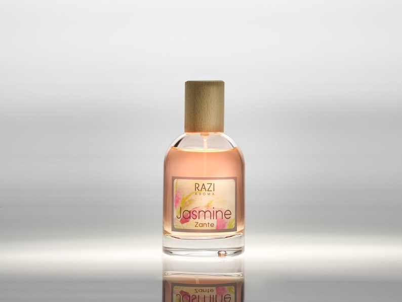 May include: A clear glass bottle with a wooden cap and a label that reads "Razi Aroma Jasmine Zante". The bottle is filled with a light pink liquid.