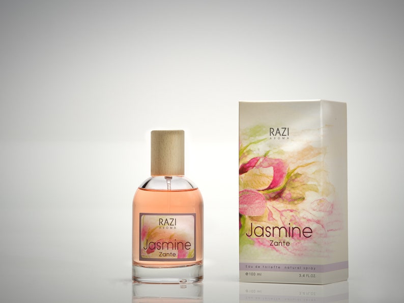 May include: A glass bottle of Jasmine Zante perfume by Razi Aroma. The bottle has a wooden cap and is filled with a light pink liquid. The label is white with pink and green floral designs and the text "RAZI Aroma Jasmine Zante Eau de Toilette Natural Spray 100 ml 3.4 fl oz."