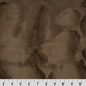 May include: A close-up of a brown faux fur fabric with a soft, plush texture. The fabric has a subtle swirl pattern and a slightly iridescent sheen.